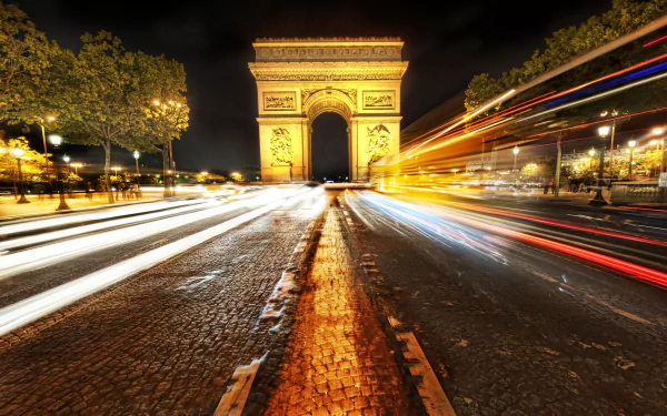 Time-lapse 4K Ultra HD image of the Arc de Triomphe at night in Paris, France, with streaks of light from passing traffic on the street.