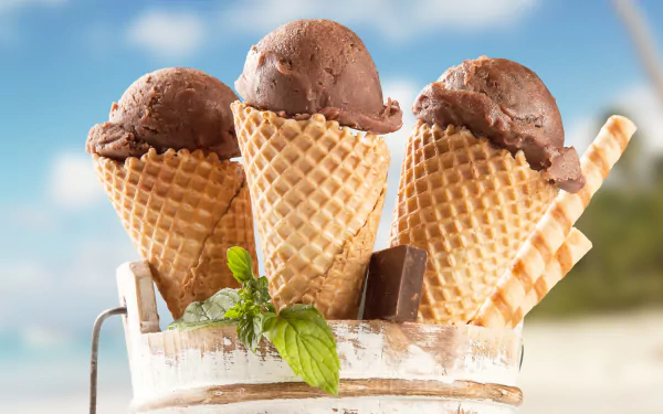 HD desktop wallpaper featuring three chocolate ice cream cones with a fresh mint garnish against a bright summer sky background.