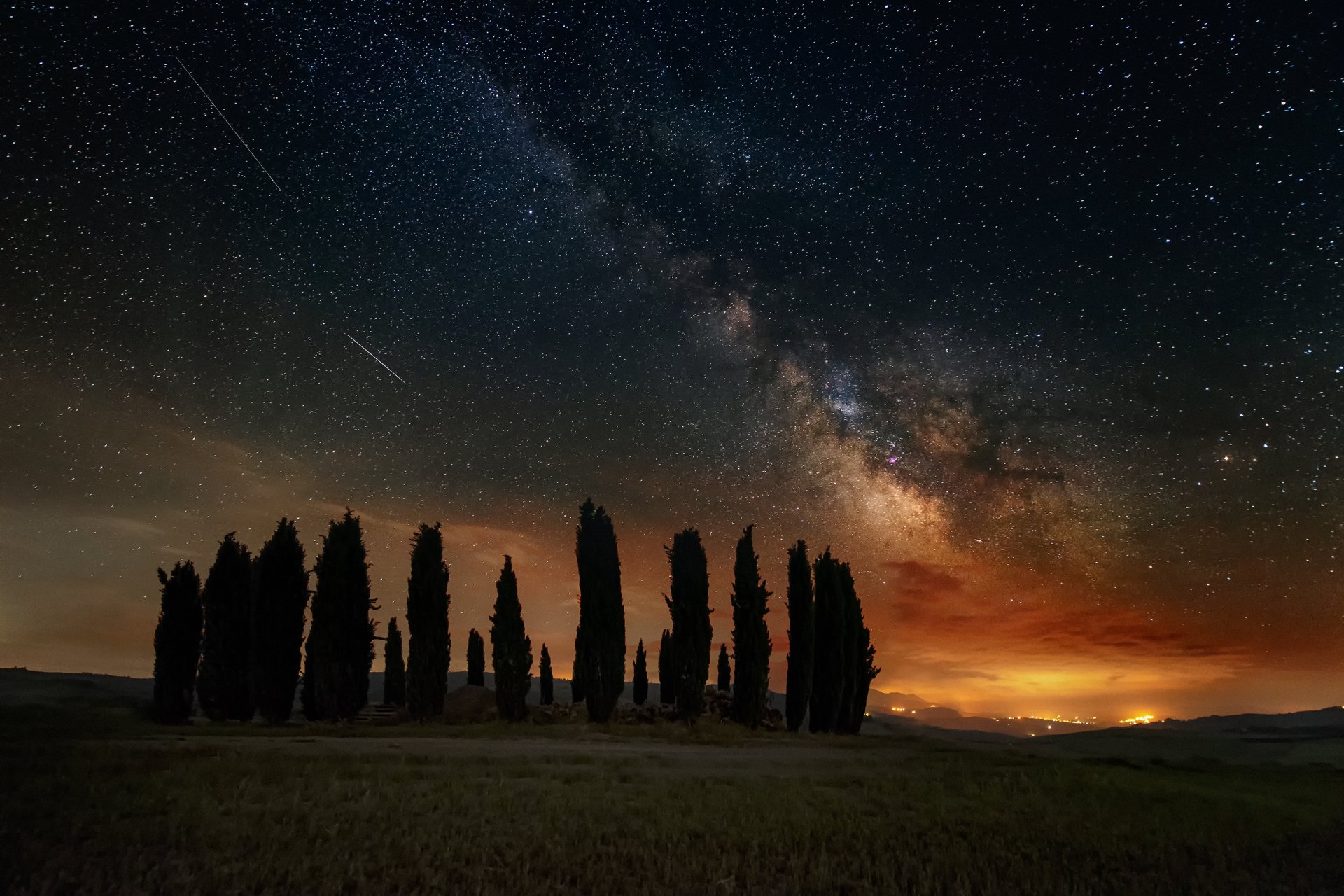 Night sky over a Tuscany landscape in Italy, featuring silhouetted trees beneath a vivid Milky Way filled with stars, creating a stunning sci-fi inspired HD desktop wallpaper.