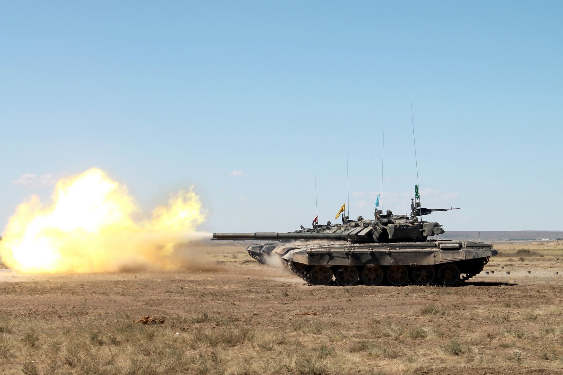 HD desktop wallpaper featuring a T-90 military tank firing on an open plain under clear blue skies.
