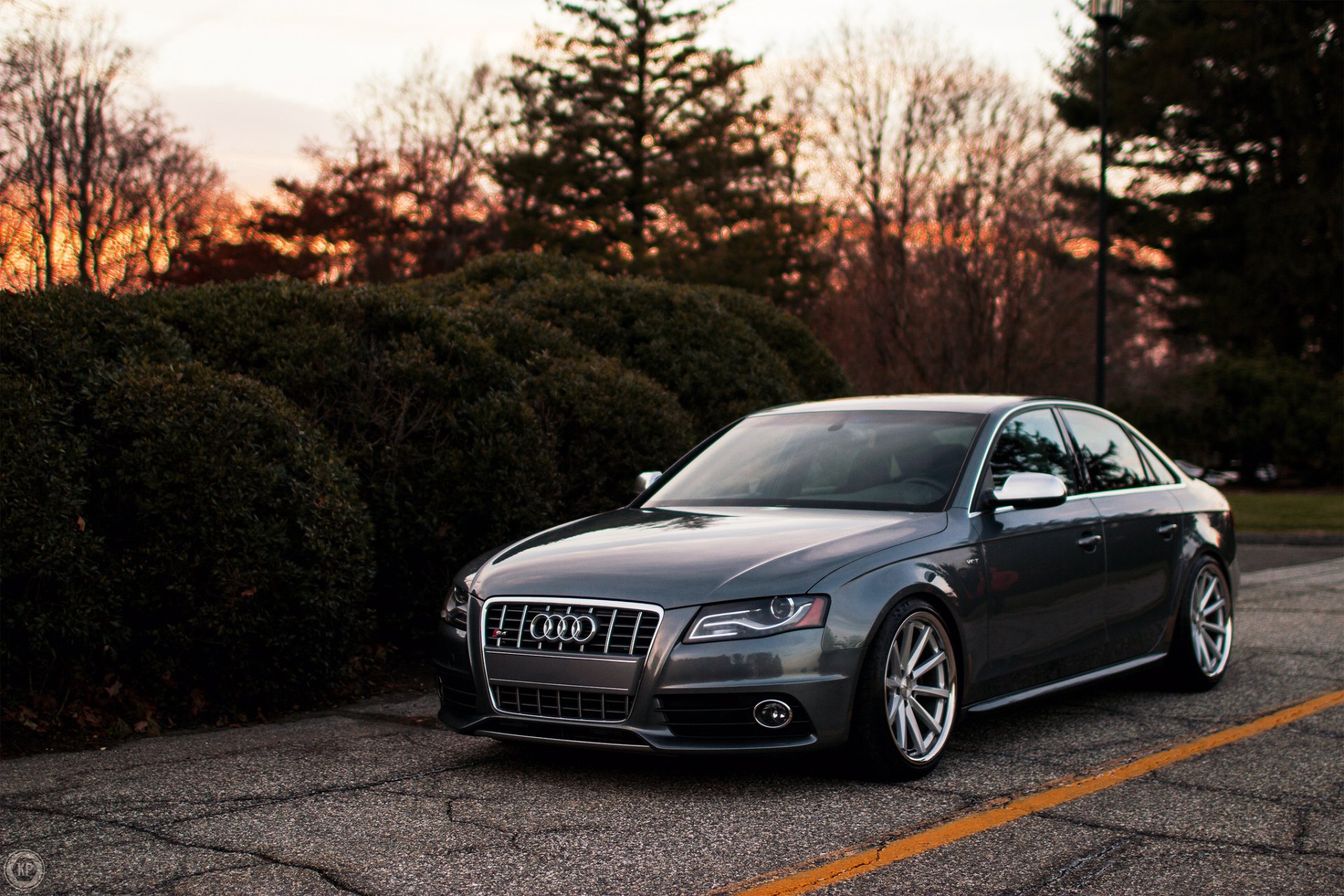 HD desktop wallpaper featuring a sleek silver Audi S4 parked on an asphalt road with trees and a sunset sky in the background.