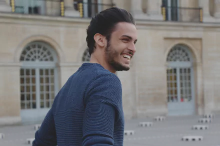 French model Baptiste Giabiconi smiles outdoors near a historic building, captured in a 4K Ultra HD PC desktop wallpaper.
