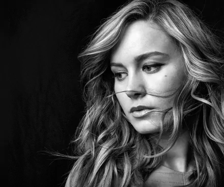 Black and white HD wallpaper featuring actress Brie Larson, capturing her contemplative expression with flowing hair against a dark backdrop.