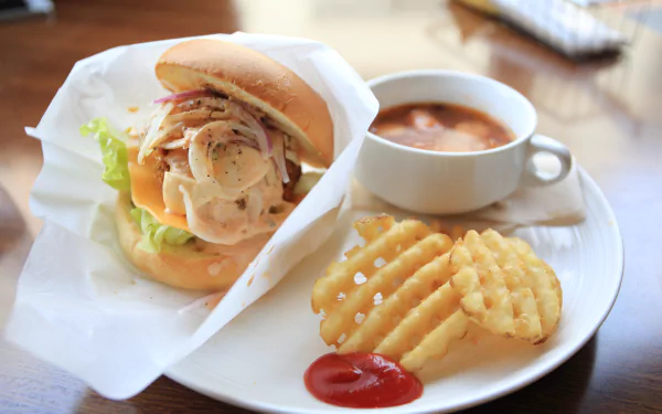 A delicious burger with fresh toppings, paired with waffle fries and a cup of soup, served on a plate. This image is a 4K Ultra HD desktop wallpaper and background.