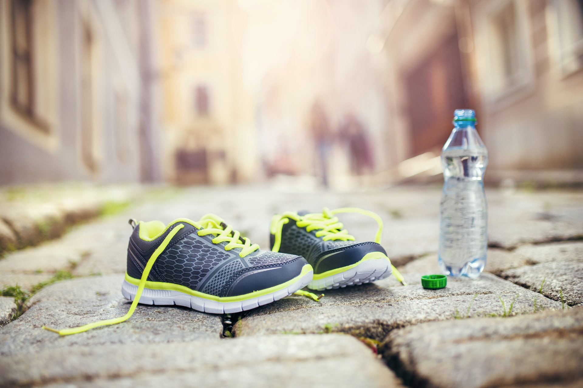 4K Ultra HD PC desktop wallpaper: bokeh city street, man-made cobblestone foreground with neon-laced running shoes and a water bottle.