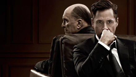 HD desktop wallpaper for The Judge (2014): two men in a wood-paneled courtroom, an older judge in robes seated back-to-back with a younger man in a suit, the younger man looking contemplative.