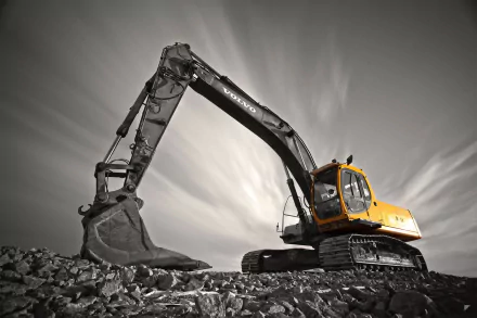 HD wallpaper of a Volvo excavator on a rocky surface with a dynamic sky in the background.