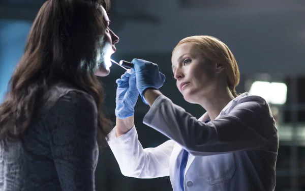 4K PC desktop wallpaper: TV sci-fi lab scene of a lab‑coat investigator examining a woman's mouth under a clinical light, tense paranormal-drama atmosphere.