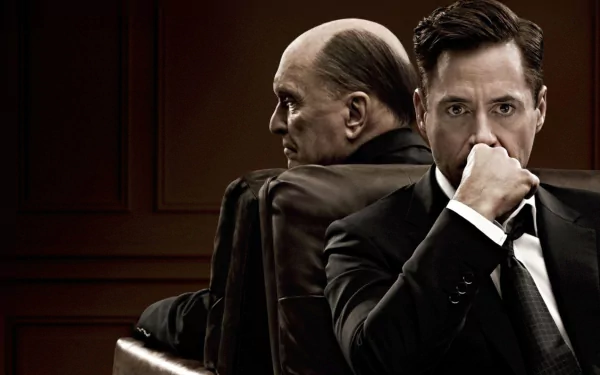 HD desktop wallpaper for The Judge (2014): two men in a wood-paneled courtroom, an older judge in robes seated back-to-back with a younger man in a suit, the younger man looking contemplative.