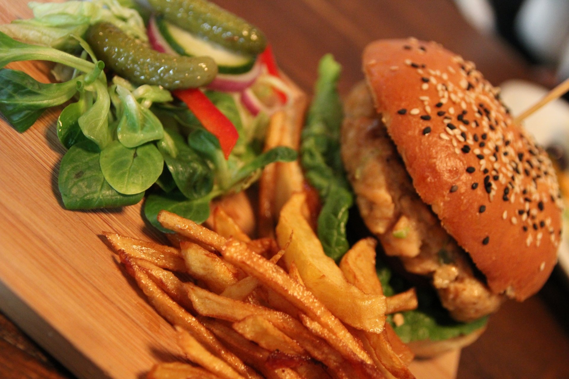 Close-up of a burger with French fries, pickles, and fresh salad on a wooden plate, captured in vibrant 4K Ultra HD quality for PC desktop wallpaper and background.