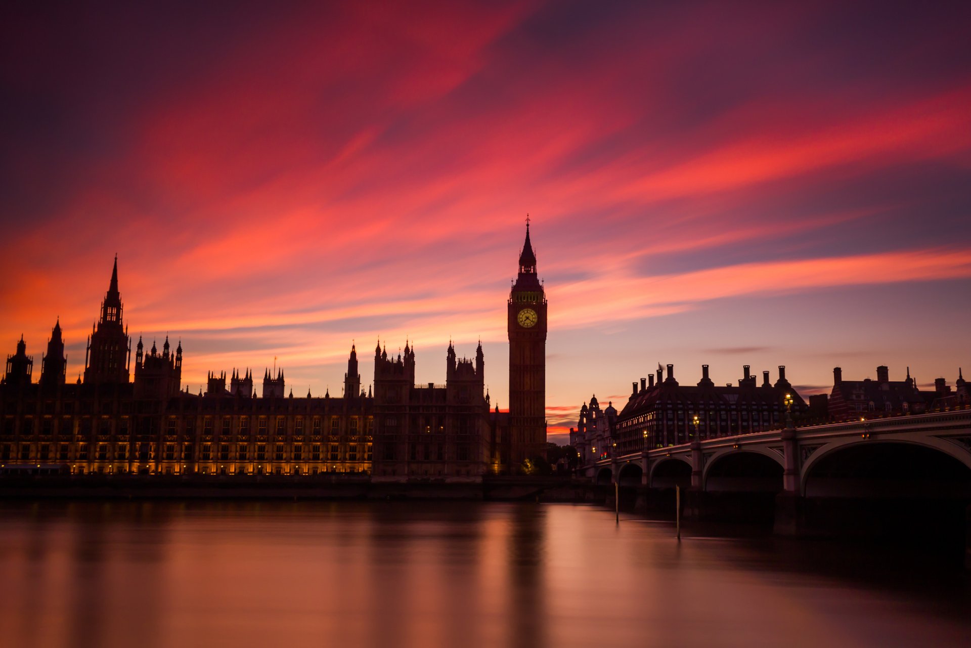 Dusk over London’s Palace of Westminster and Big Ben, with the river Thames and a bridge reflecting vibrant colors in the sky.