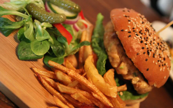 Close-up of a burger with French fries, pickles, and fresh salad on a wooden plate, captured in vibrant 4K Ultra HD quality for PC desktop wallpaper and background.