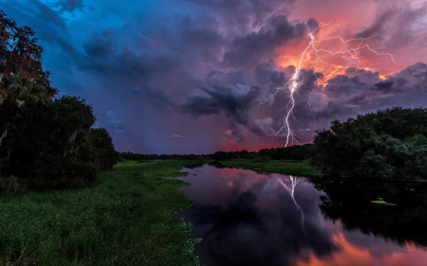 A dramatic stormy sky with dark clouds and lightning reflects in a calm river, surrounded by lush greenery, creating a striking contrast between light and shadow.