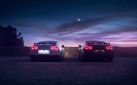 HD PC desktop wallpaper featuring two Nissan GT-R vehicles parked side by side under a twilight sky with a crescent moon.