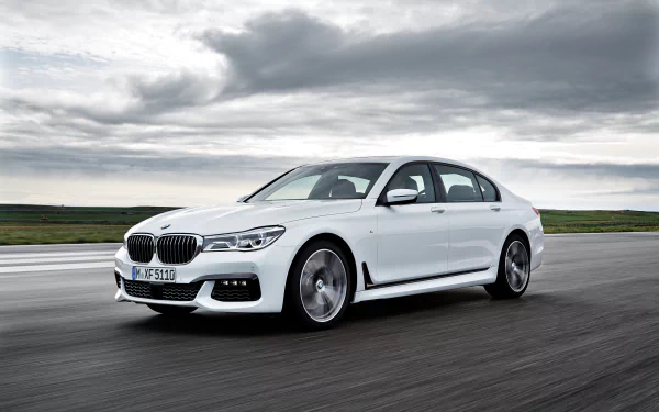A sleek white BMW 7 Series drives on an open road, showcasing its elegant design against a backdrop of moody skies in this stunning 4K Ultra HD wallpaper.