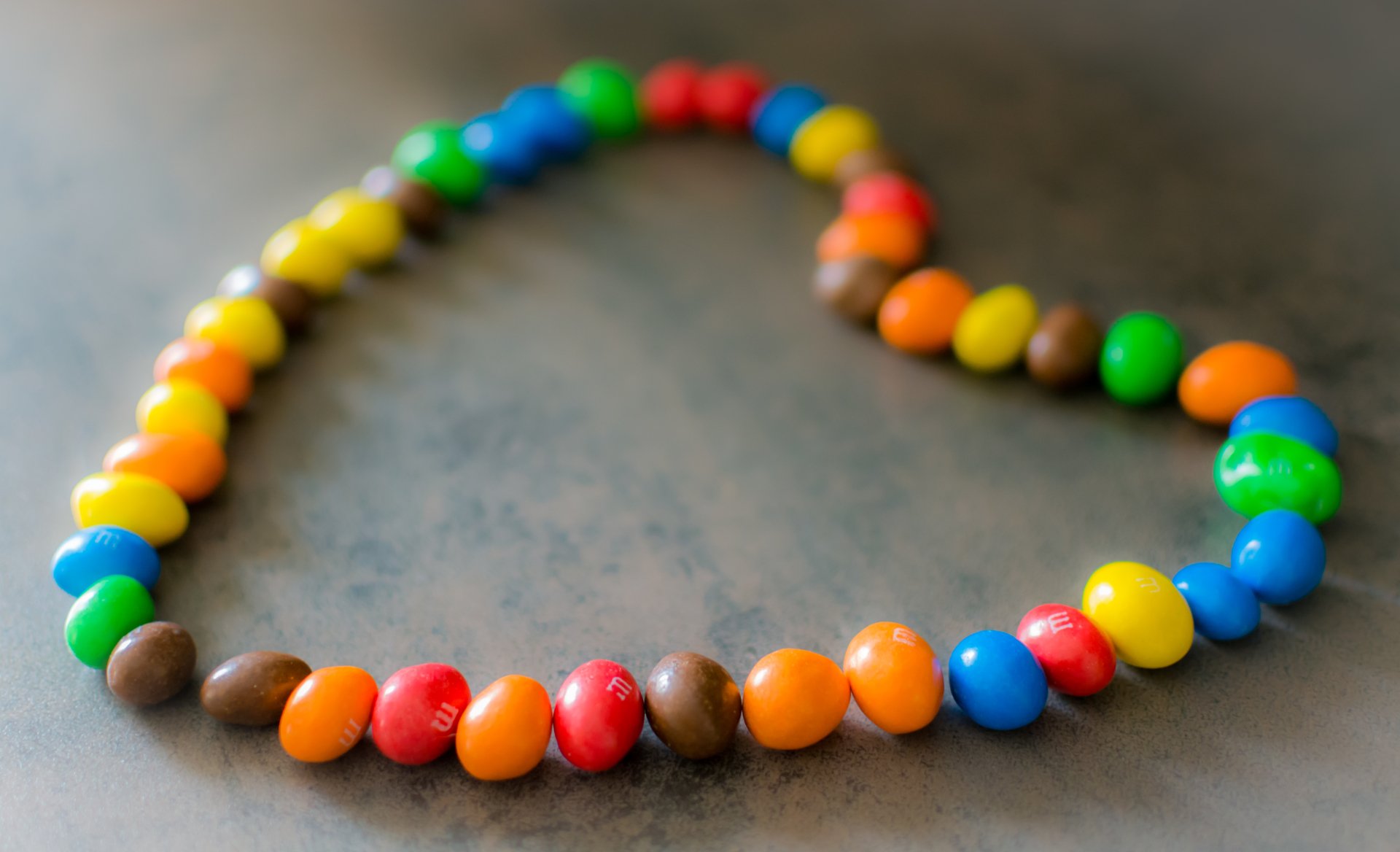 A heart shape formed from colorful M&M's candy pieces on a surface, captured in 4K Ultra HD as a vibrant PC desktop wallpaper.