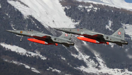 Two military Northrop F-5 jet fighters with red external tanks fly over snow-covered mountains — 2K Quad HD PC desktop wallpaper/background of warplane aircraft.