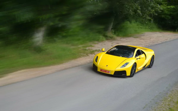 A yellow Spania GTA Spano supercar speeds along a tree-lined road, captured in high definition as a vibrant desktop wallpaper and background image.