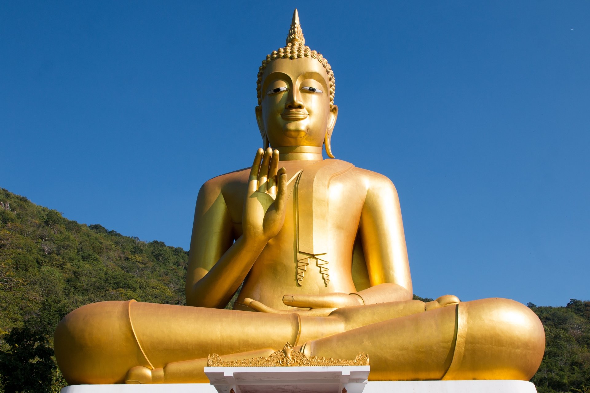 HD desktop wallpaper featuring a golden Buddha statue in a serene outdoor setting against a clear blue sky, symbolizing Buddhism and religious peace.