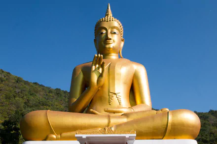 HD desktop wallpaper featuring a golden Buddha statue in a serene outdoor setting against a clear blue sky, symbolizing Buddhism and religious peace.