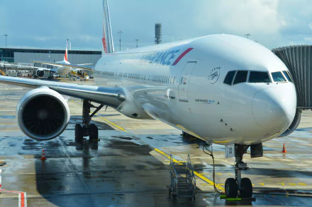 A Boeing 777 aircraft is parked at the airport, showcasing its sleek design and vibrant livery, set against a backdrop of terminal infrastructure and bright skies.