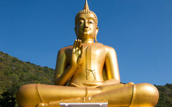 HD desktop wallpaper featuring a golden Buddha statue in a serene outdoor setting against a clear blue sky, symbolizing Buddhism and religious peace.