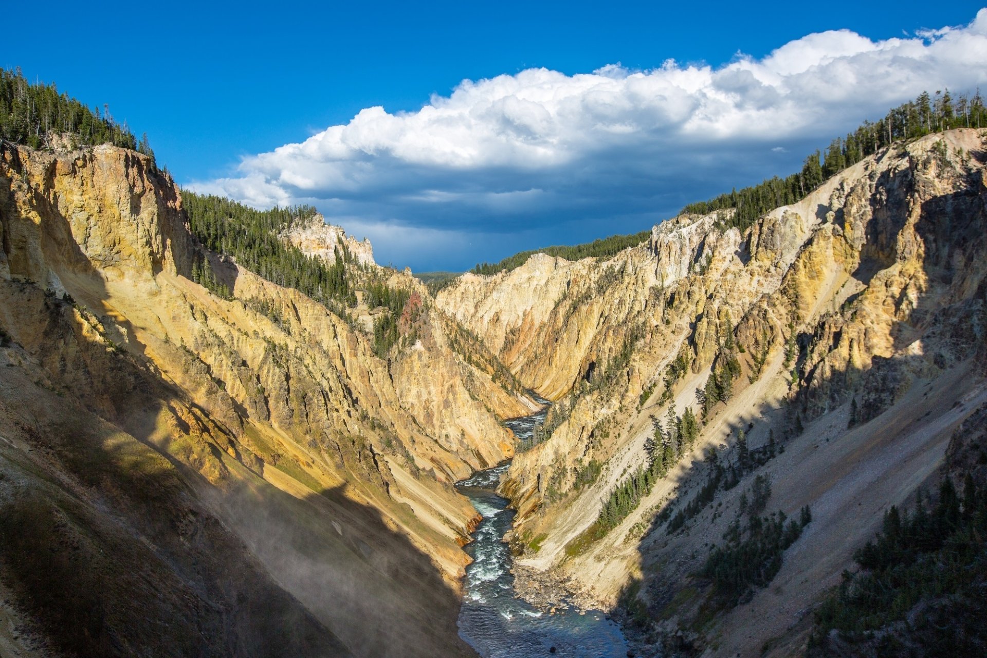 A breathtaking panorama of Yellowstone National Park showcasing a canyon and river flowing through a scenic valley, framed by towering cliffs and dramatic clouds above.