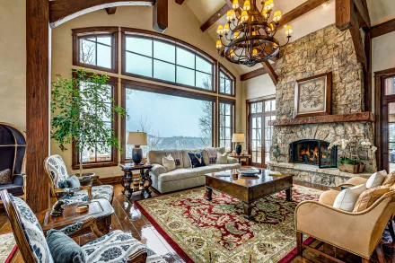 A cozy lounge featuring a stone fireplace, chandelier, and elegant furnishings, with a potted plant and a coffee table that adds charm to the inviting ambiance.