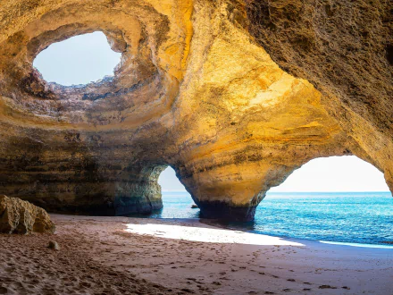 HD PC wallpaper of a sunlit natural cave in Portugal, showcasing rugged rock formations opening to the blue ocean and bright sky beyond.
