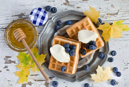 HD desktop wallpaper featuring blueberry-topped waffles with honey and ice cream, surrounded by fresh blueberries and autumn leaves on a rustic wooden table.
