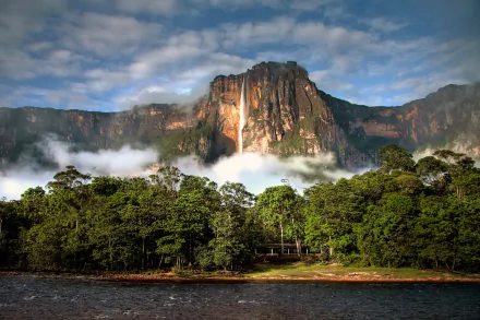 A breathtaking view of Angel Falls in Venezuela, showcasing a majestic waterfall cascading down a cliff, surrounded by lush greenery and misty clouds over the serene water.