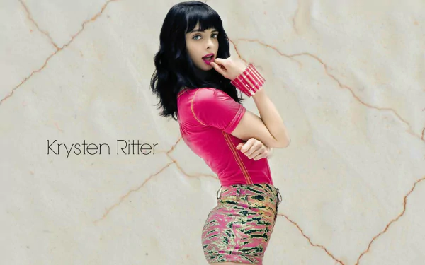 HD desktop wallpaper featuring celebrity Krysten Ritter with black hair, wearing a pink top and patterned skirt against a light marble background.