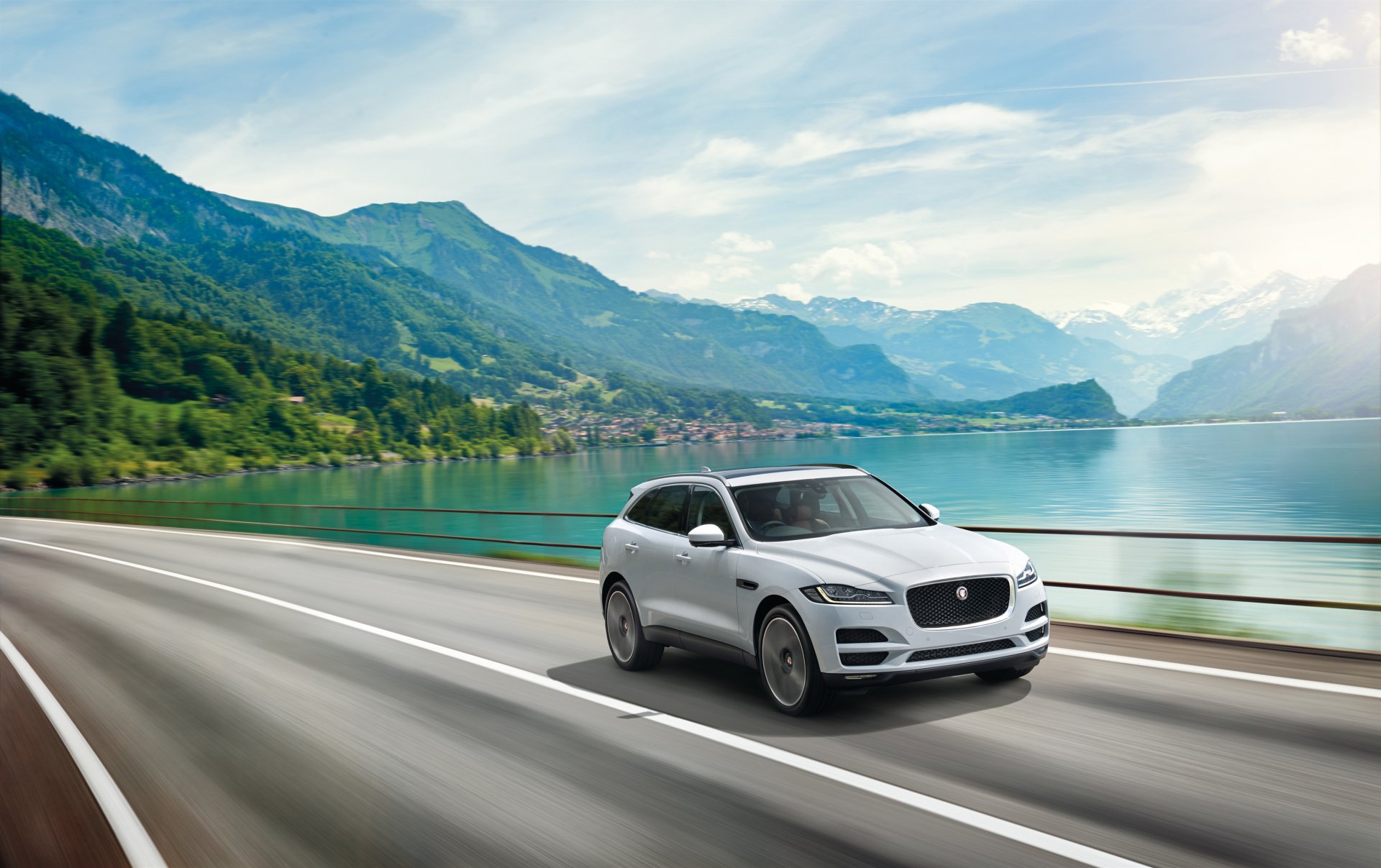 White Jaguar F-PACE SUV driving on a scenic mountain road by a lake, captured in a sharp 4K Ultra HD desktop wallpaper background.