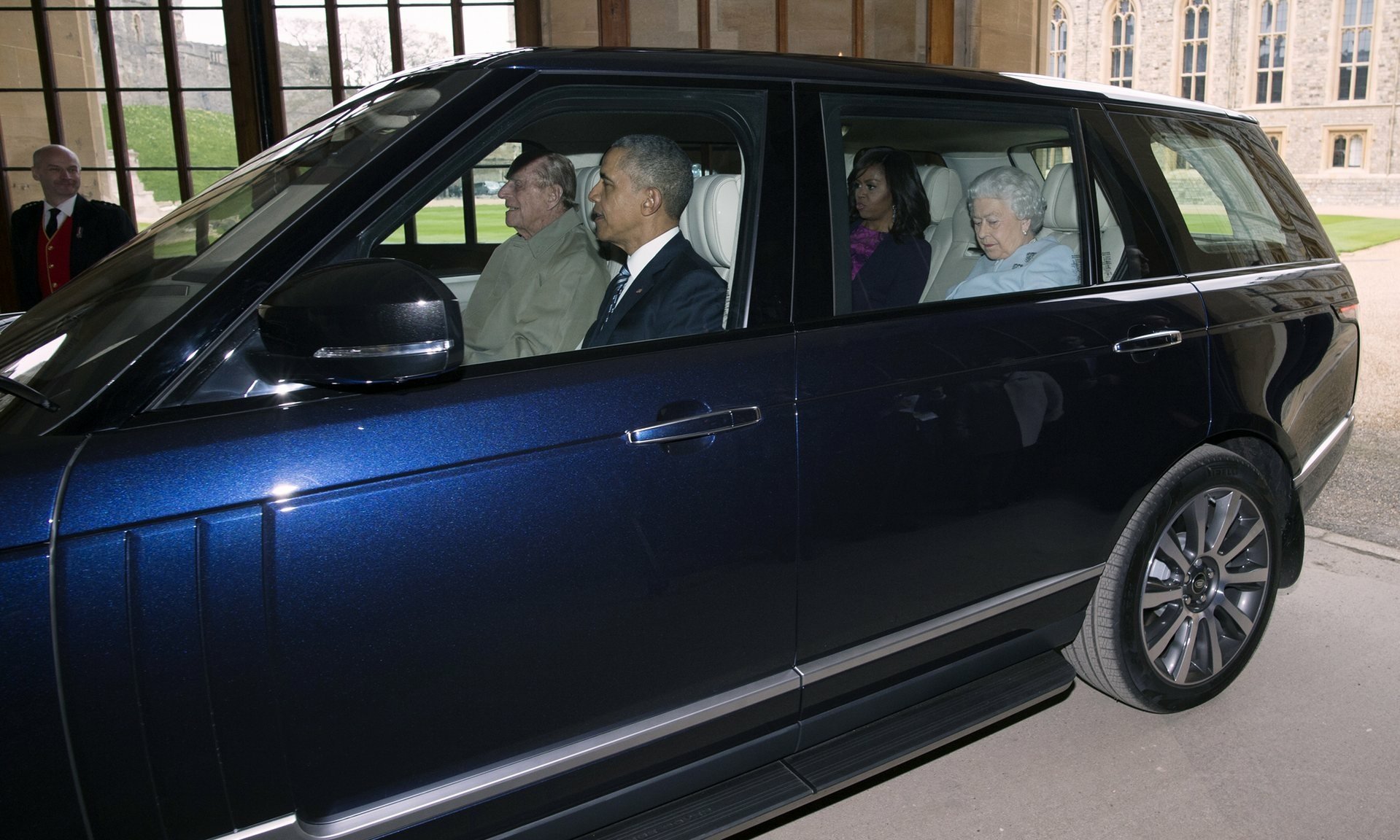 HD desktop wallpaper featuring Queen Elizabeth II and others seated inside a black luxury car, captured outside a historic building.