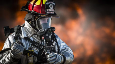 HD desktop wallpaper of a firefighter wearing a gas mask and helmet, ready for action against a smoky, fiery background.
