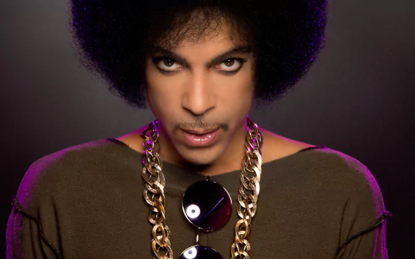 HD desktop wallpaper of American singer Prince with brown eyes, an afro hairstyle, sunglasses hanging on a gold chain, and intense gaze under soft lighting.