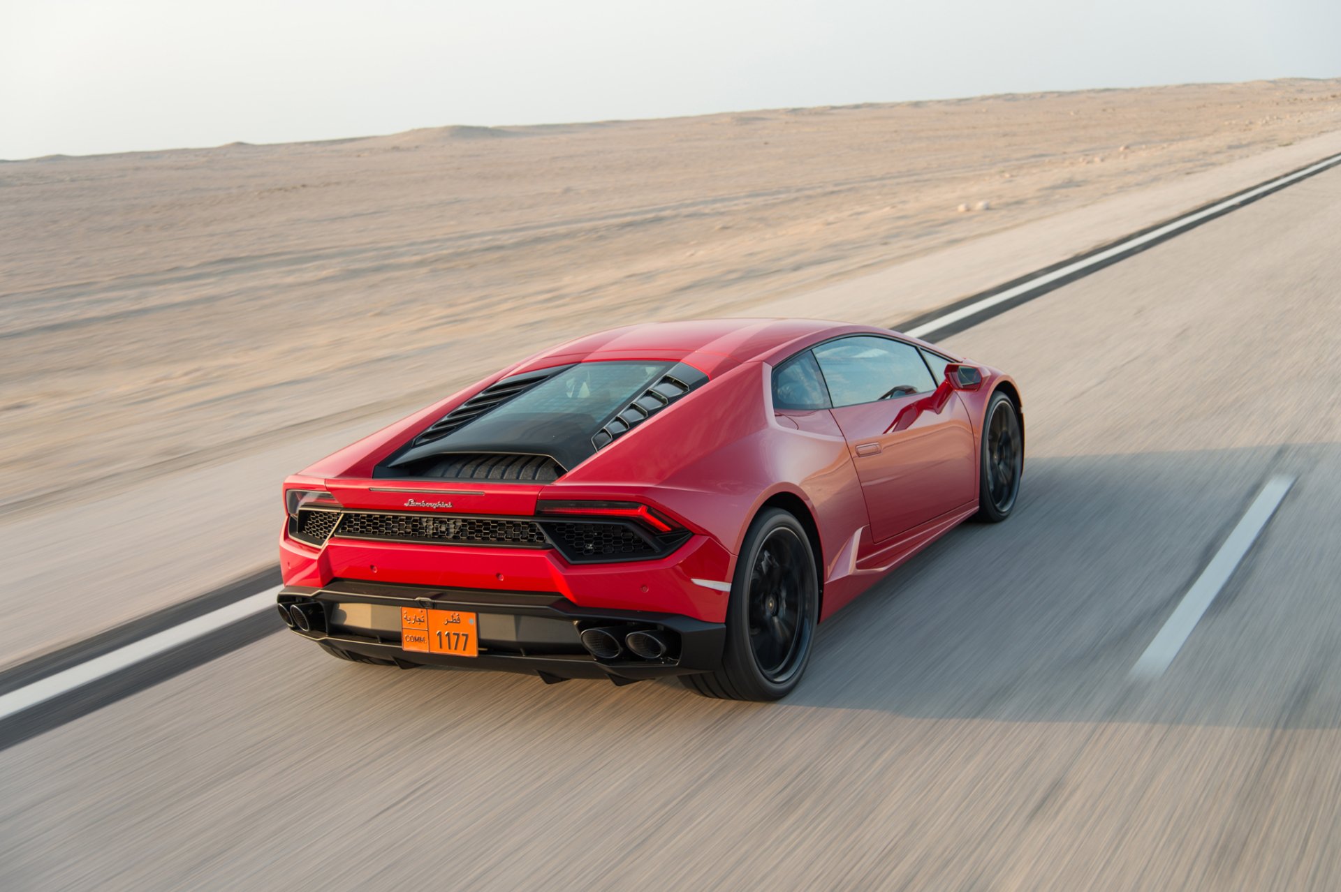 HD desktop wallpaper featuring a red Lamborghini Huracan supercar driving on a desert road, showcasing its sleek design and dynamic performance.