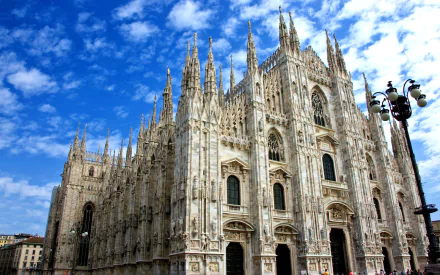 HD PC desktop wallpaper of Milan Cathedral, Milan, Italy — Gothic church architecture with ornate spires and carved façade beneath a bright blue sky, a religious cathedral landmark.