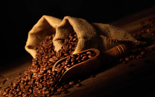 5K Ultra HD PC desktop wallpaper of roasted coffee beans (food/coffee) spilling from burlap sacks with a wooden scoop, bathed in warm, rich brown tones.