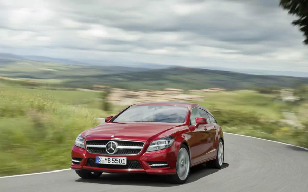 Red Mercedes-Benz CLS500 from the CLS-Class drives on a winding road with scenic countryside in the background, showcased as an HD PC desktop wallpaper.