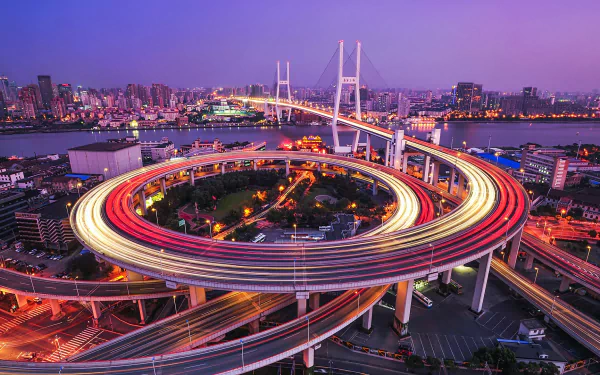 Time-lapse view of Nanpu Bridge’s circular highway ramp in Shanghai, China, showcasing vibrant cityscape and illuminated roads at twilight.