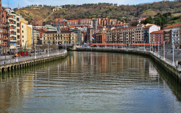 4K Ultra HD view of a man-made waterfront in Bilbao, Spain, showcasing urban buildings and cityscape along a calm river with hills in the background.