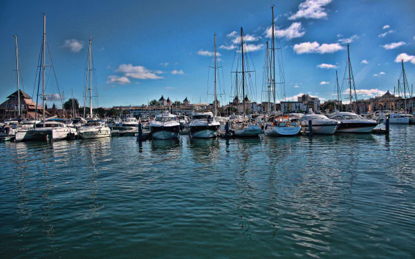 4K Ultra HD desktop wallpaper of Portimão harbor in Portugal: row of moored sailboats and yachts on calm sea under a blue sky, man-made marina and waterfront buildings.