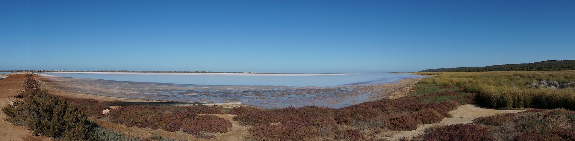 HD PC desktop wallpaper showcasing a serene lagoon surrounded by dry, earthy vegetation under a clear blue sky.