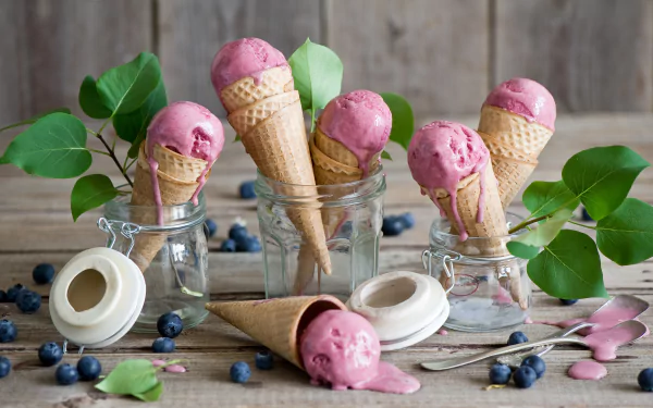 A vibrant still life featuring ice cream cones with blueberry-flavored ice cream, surrounded by fresh blueberries and green leaves, set against a rustic wooden background.