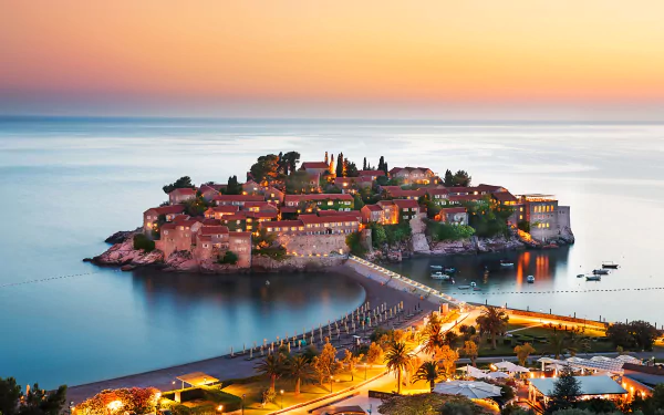 HD desktop wallpaper capturing a man-made island resort and town in Montenegro, featuring illuminated houses and a connecting walkway at sunset.