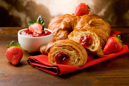 A delicious breakfast scene featuring flaky croissants filled with strawberry jam, fresh strawberries, and a bowl of jam, all set on a vibrant red napkin against a warm wooden backdrop.