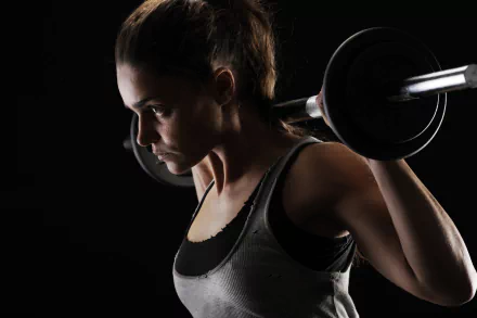 A brunette woman with brown eyes lifts a barbell, captured in sharp detail against a dark background in this 4K Ultra HD sports-themed wallpaper.