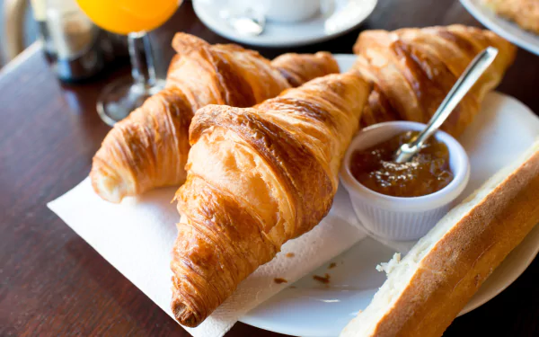 Close-up of flaky croissants served with jam and a baguette on a breakfast table, captured in vibrant 4K Ultra HD detail for a PC desktop wallpaper.