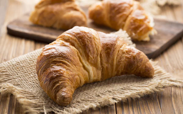 Golden flaky croissants on burlap and a wooden board, breakfast food close-up — 5K Ultra HD PC desktop wallpaper and background.